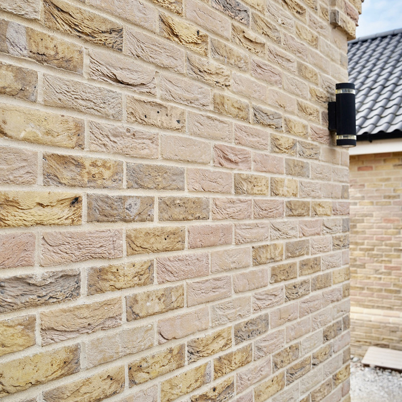 Close-up of a modern house exterior showcasing mixed-tone buff and tan brick style with rough and smooth textures under natural daylight.