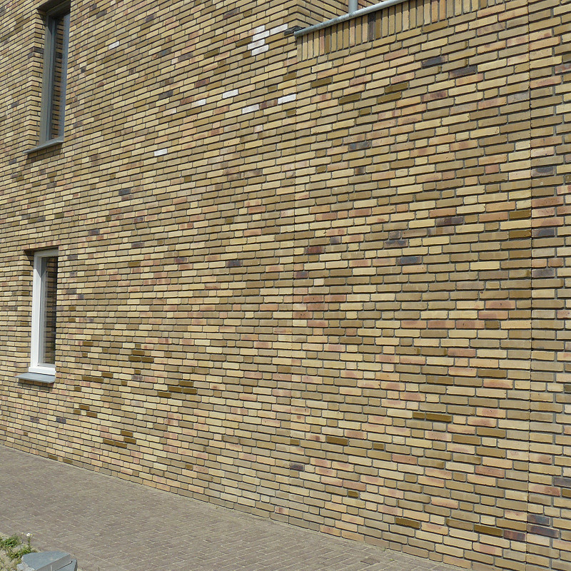 Yellow-toned brick wall with a mix of beige, tan, and occasional darker bricks, featuring a single narrow window with a white frame and grey windowsill.