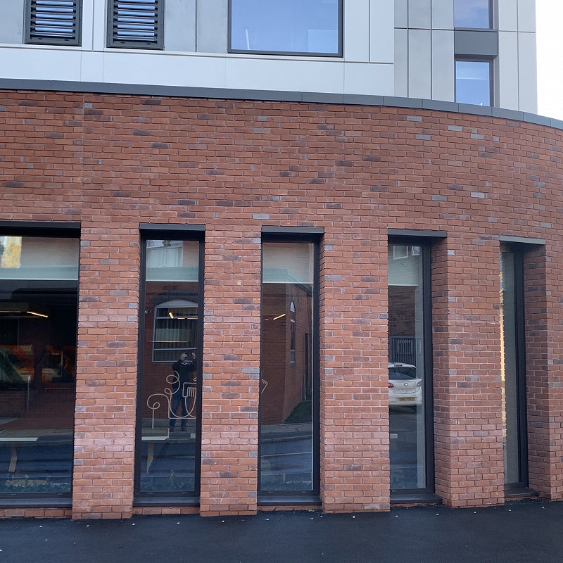 Modern red brick building with curved architecture and tall vertical windows, showcasing urban design and clean, contemporary style.